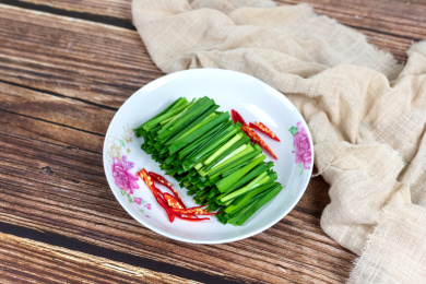 木纹桌子上白色盘子里的绿色韭菜食材