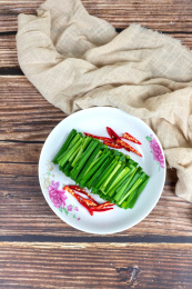 木纹桌子上白色盘子里的绿色韭菜食材