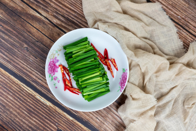 木纹桌子上白色盘子里的绿色韭菜食材