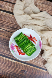 木纹桌子上白色盘子里的绿色韭菜食材