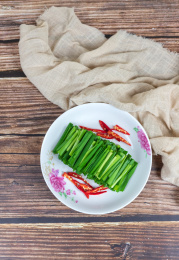 木纹桌子上白色盘子里的绿色韭菜食材