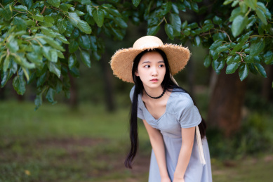 身穿蓝色的长裙的漂亮女生站在树底下