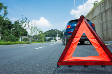远处的路边停着一辆坏掉的汽车，车后面放着一个三角警告牌