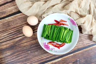 木桌上的两个鸡蛋和白色盘子里的绿色韭菜