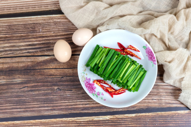 木桌上的两个鸡蛋和白色盘子里的绿色韭菜