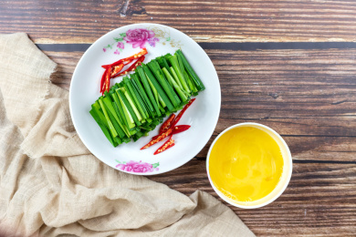 木桌上白色盘子里的绿色韭菜和小碗里的鸡蛋清