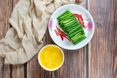 木桌上白色盘子里的绿色韭菜和小碗里的鸡蛋清