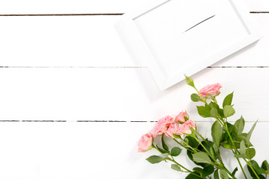 白色木桌面上的一束粉色蔷薇鲜花和一个白色相框