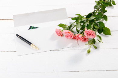 白色木桌面上的信封和一束粉色蔷薇鲜花