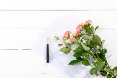 白色木桌面上的信纸上的一束粉色蔷薇鲜花