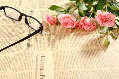 放在旧报纸上的一束粉色鲜花蔷薇和眼镜