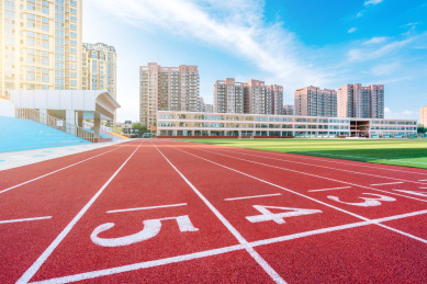阳光下的体育场红色跑道和远处的高楼建筑