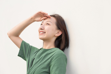 单手放在额头上遮挡阳光的亚裔女人在纯色背景墙前