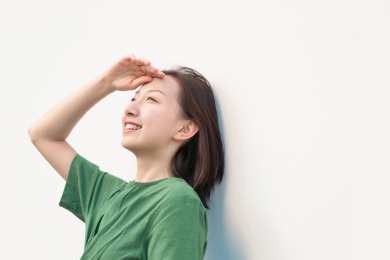 单手放在额头上遮挡阳光的亚裔女人在纯色背景墙前