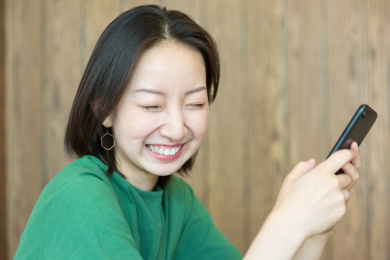 手握智能手机眯起眼睛大笑的亚裔女人