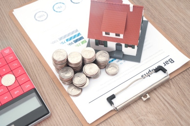 金融文件上的小房子模型和美元硬币及旁边一个计算器