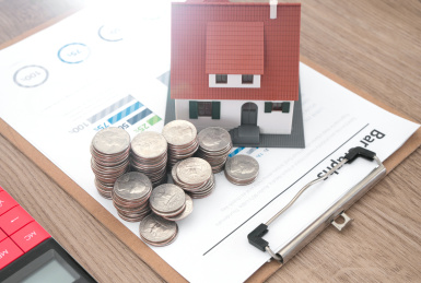 金融文件上的小房子模型和美元硬币及旁边一个计算器