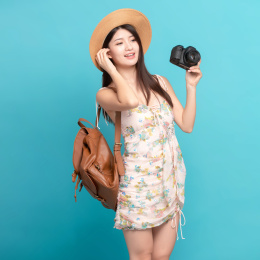蓝色背景里，手上拿着单反相机的美丽亚洲女孩