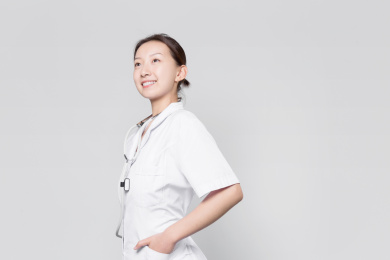 站在灰色背景前自信微笑的女医生双手插袋目视远方