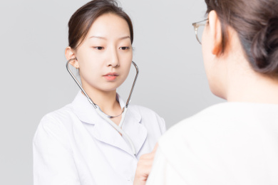浅灰色背景前一名年轻漂亮的女医生在给一位患者看病