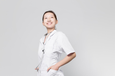 站在灰色背景前自信微笑的女医生双手插袋目视远方