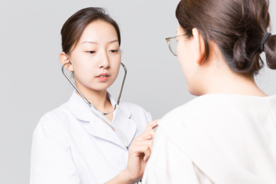 浅灰色背景前一名年轻漂亮的女医生在给一位患者看病