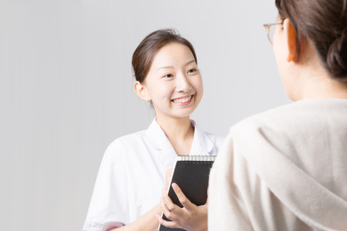 浅灰色背景前一名年轻漂亮的女医生在给一位患者看病