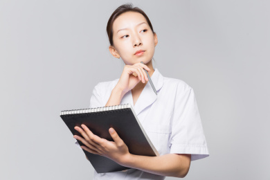 站在灰色背景前侧身看镜头的女医生手拿本子和笔正在微笑