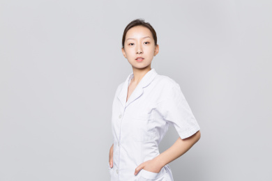 一位年轻的女医生站在灰色背景墙前双手插袋看镜头