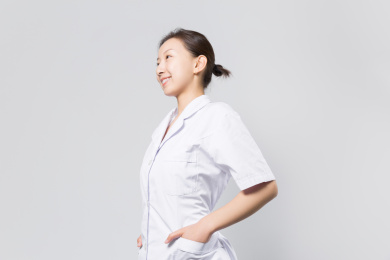一位年轻的女医生站在灰色背景墙前双手插袋