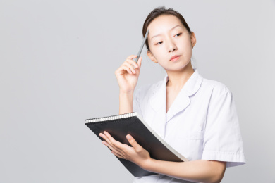 站在浅灰色背景前把笔放在头上手拿文件的女医生正在思考