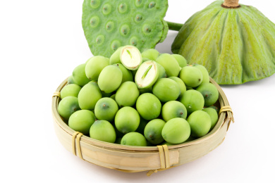 白色背景上放着一个莲蓬和一筐莲子，莲子上面放着一颗切开了能看到莲心的莲子