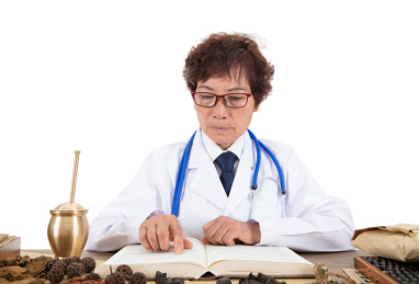 穿着白大褂的中国老中医在放满草药的桌子上认真看书
