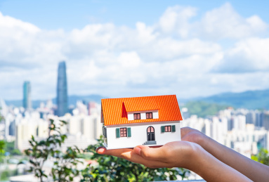 双手捧着小房子模型和城市建筑风光背景