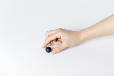 白色背景一只手拿着一颗中成药药丸特写