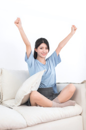 坐在白色沙发上，抱着枕头的年轻的亚洲女孩