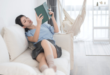 躺在白色沙发上，正在看书的东方女孩