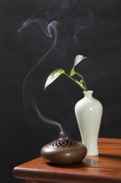 深色背景前摆放在红木桌面上的紫铜香炉