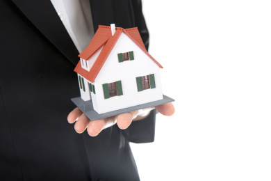 房地产销售人员手托小房子模型站在白背景前