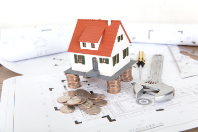 工程施工图纸上被硬币垫起来的小房子模型和几个施工工具