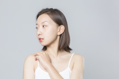 一只手放在肩膀锁骨位置脸看向一旁的亚洲女孩站在纯色背景墙前