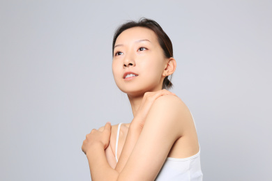 一位美丽亚裔女孩环抱肩膀站在纯色背景墙前