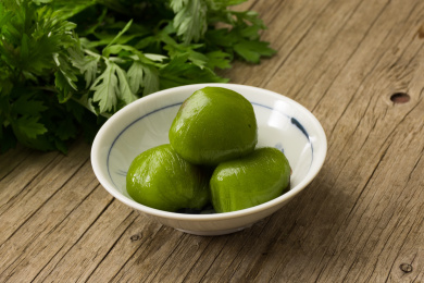 一个碗里装着三个传统美食青团，旁边放着植物艾草