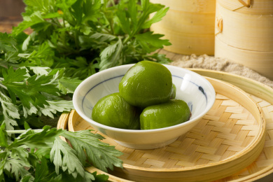 放在碗里的传统美食青团，旁边还放着新鲜植物艾草