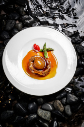 白色瓷盘装的南非干鲍摆放在水中鹅卵石上