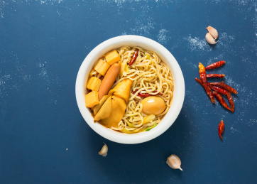 一碗刚出锅的牛肉板面放在蓝色木板上桌面上还有蒜瓣和川椒