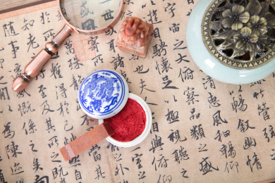 俯视拍摄书桌上铺开的书法作品和篆刻印章及打开的印泥和一把放大镜