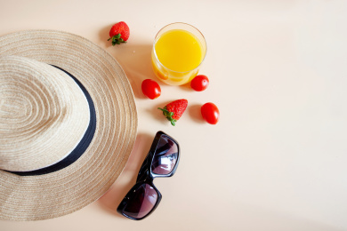 新鲜水果草莓和小番茄与透明的杯子，橙汁，墨镜，草帽和纯色的背景