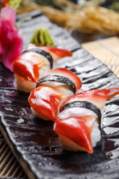 黑色长瓷盘装的北极贝手握寿司摆放在寿司帘上