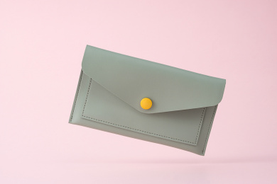 粉色背景前，掉落的绿色时尚小皮包